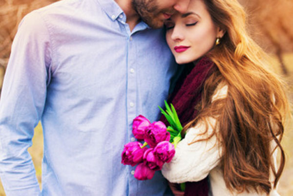 Парень обнимает девушку. Она к нему прижимается. В руке у девушки букет цветов