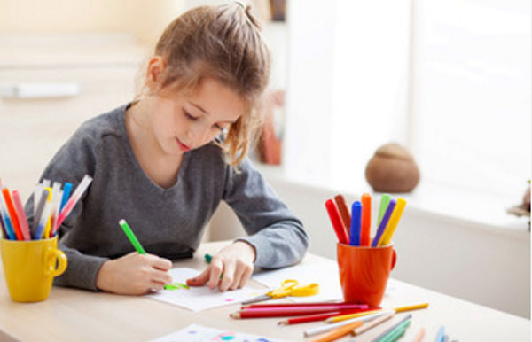 Девочка сидит за столом и что-то рисует