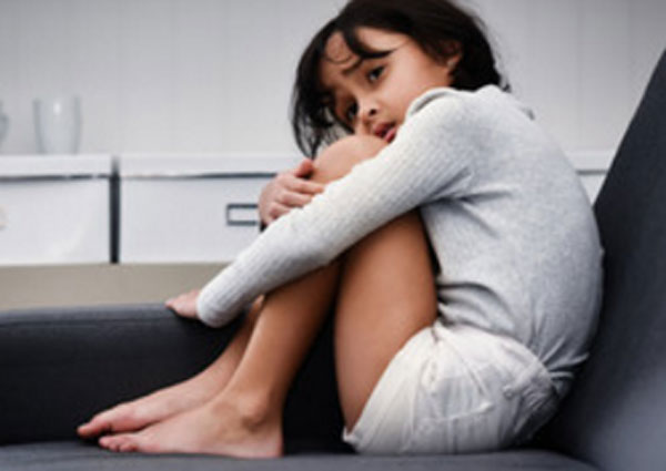 Ребенок сидит на кровати, подогнув ноги.