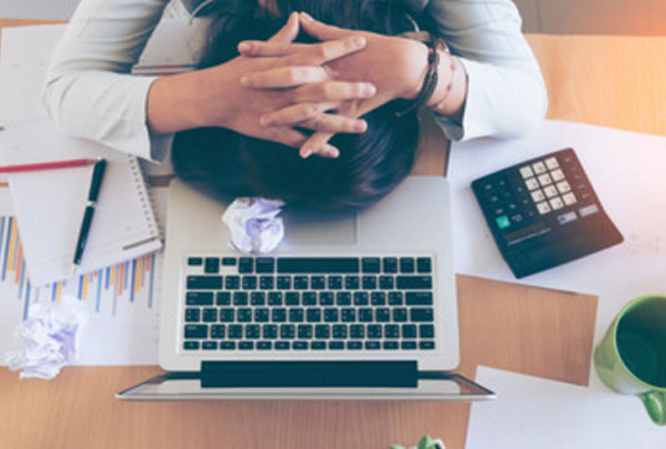 Женщина лежит лицом на столе. Рядом ноутбук, калькулятор, блокнот с ручкой