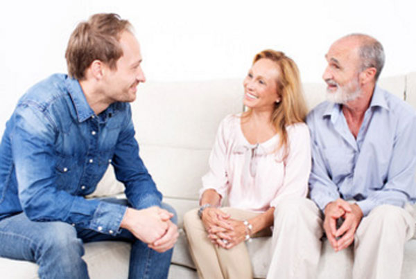 Мужчина сидит на диване с женщиной и пожилым мужчиной. Они общаются