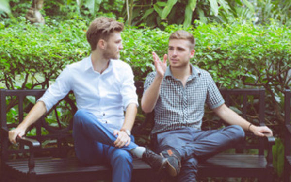 Мужчина что-то рассказывает и показывает другому мужчине, сидя на скамье