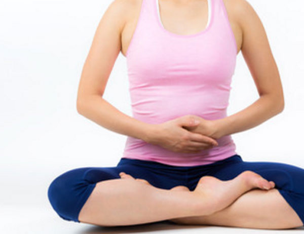 Девушка сидит в позе лотоса. Держит руками живот