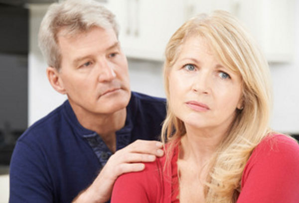 Женщина сидит рядом с мужчиной. Он держит ее за плечо. В глазах женщины грусть