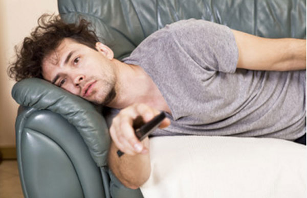 Парень лежит на диване с пультом в руках
