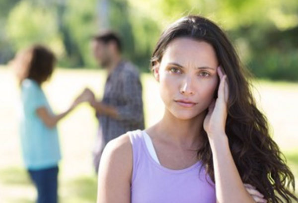 Женщина держится за голову. На задем плане мужчина беседует с женщиной, взявшись за руки