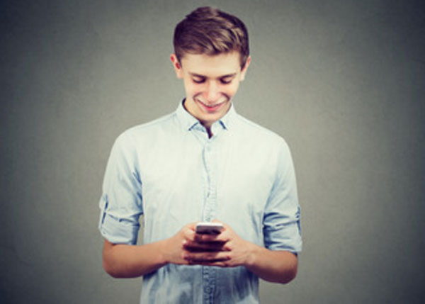 Парень пишет сообщение на смартфоне и улыбается