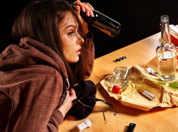 Девушка с бутылкой в руке. На столе пустая бутылка от спиртного, сигареты, таблетки