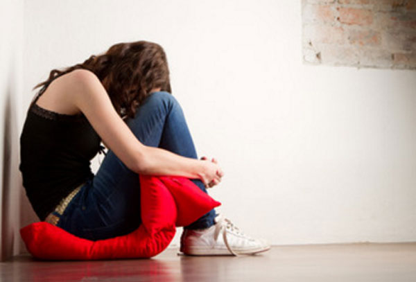 Девочка сидит на полу на подушке. Она прижала голову к коленкам